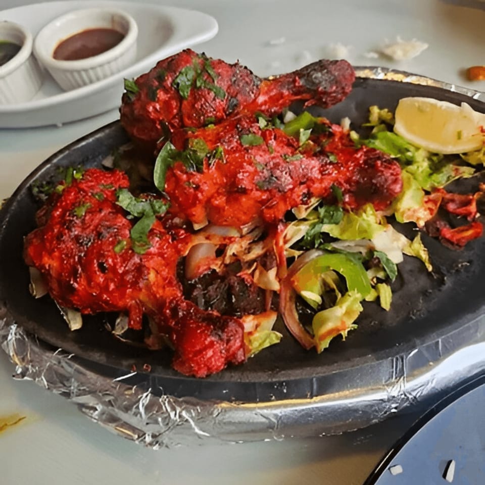 Tandoori chicken drumsticks with fresh greens and a lemon wedge on a sizzling platter at THE CHENNAI CAFE.