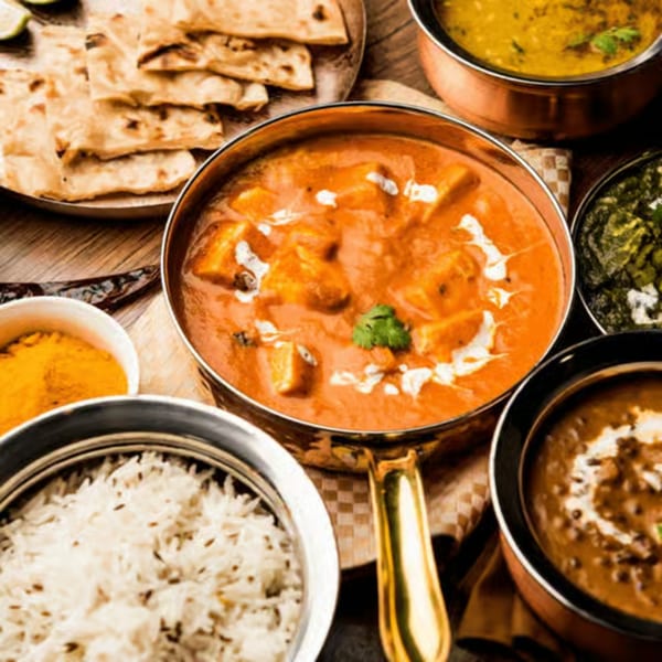 A spread of Indian dishes including paneer butter masala, dal, rice, and naan bread.